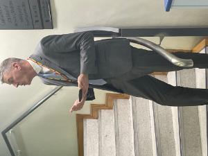 Rory Breathnach in a grey suit and rainbow lanyard speaks on the staircase